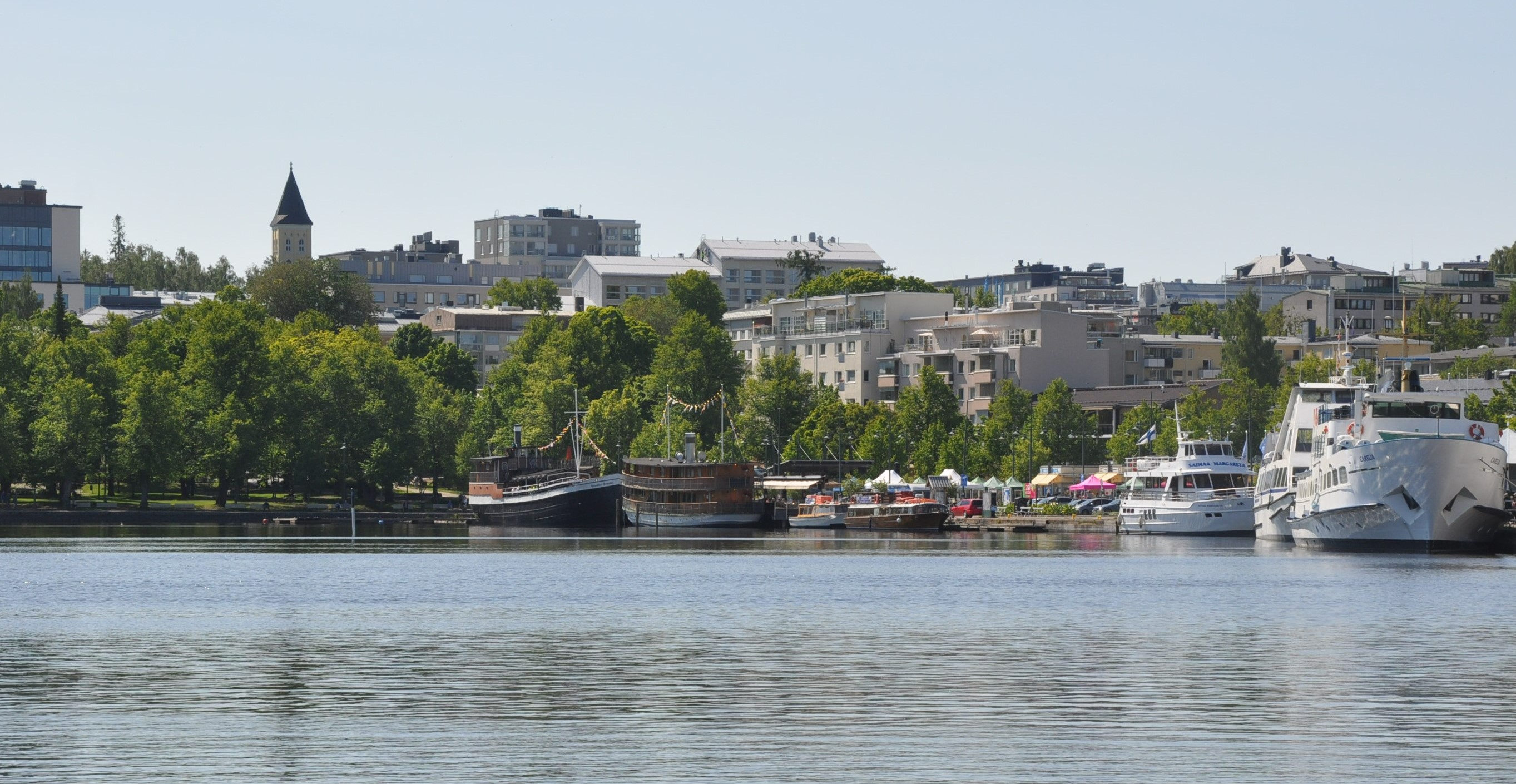 Lappeenrannan satama kaupunginlahdelta kuvattuna. Etualalla laivoja, taustalla vihreitä puita ja keskustan rakennuksia.