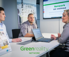 Kaksi miestä ja nainen neuvotteluhuoneen pöydän ääressä. Taustalla Greenreality Network -materiaaleja.