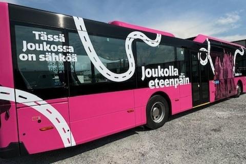 Pink electric bus, which has texts "Tässä Joukossa on sähköä" and "Kuljetaan Joukolla"