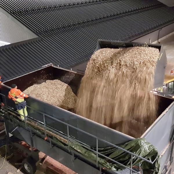 Wood chips are being poured into a silo at an energy plant, in the foreground an employee wearing a safety coverall is monitoring the situation.